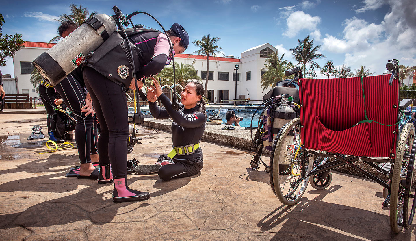 小兒麻痺的潛水教練正幫聽障學員檢查裝備。(攝影／台灣身心障礙潛水協會)
