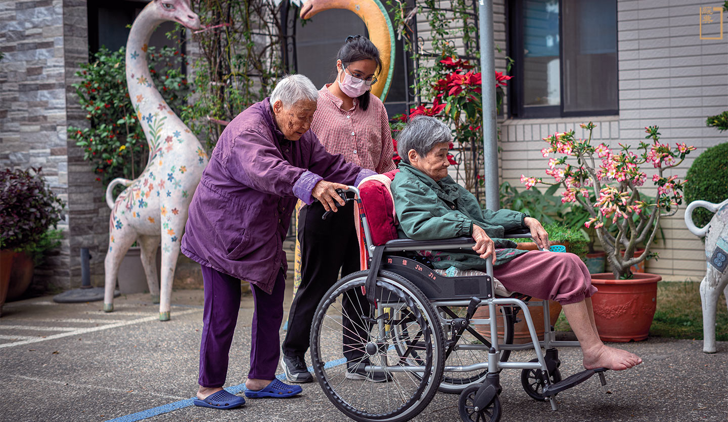 在高雄市宏仁老人長期照顧中心，熱心助人的阿玉阿嬤推著另一位阿嬤到庭園散步。(攝影／安培淂)